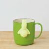 Green mug with whimsical figure tea infuser, ideal for fun and unique tea time.