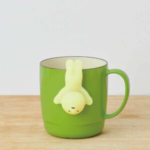 Green mug with whimsical figure tea infuser, ideal for fun and unique tea time.