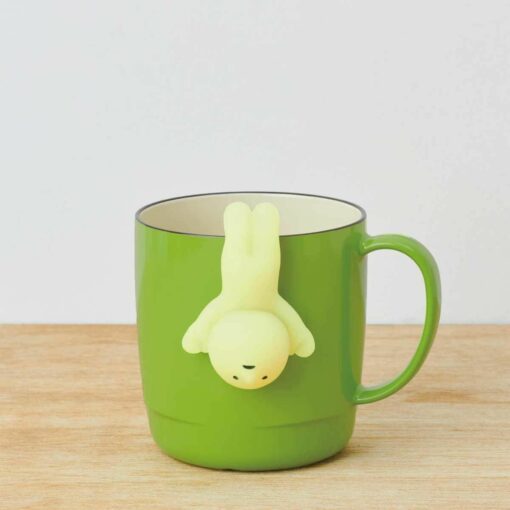 Green mug with whimsical figure tea infuser, ideal for fun and unique tea time.