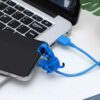 Blue dog-shaped USB cable protector for smartphone charging, connected to laptop. Prevents cable damage.