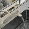 Expandable dish rack with water drainage spout over sink, featuring stainless steel frame and space for kitchen accessories.